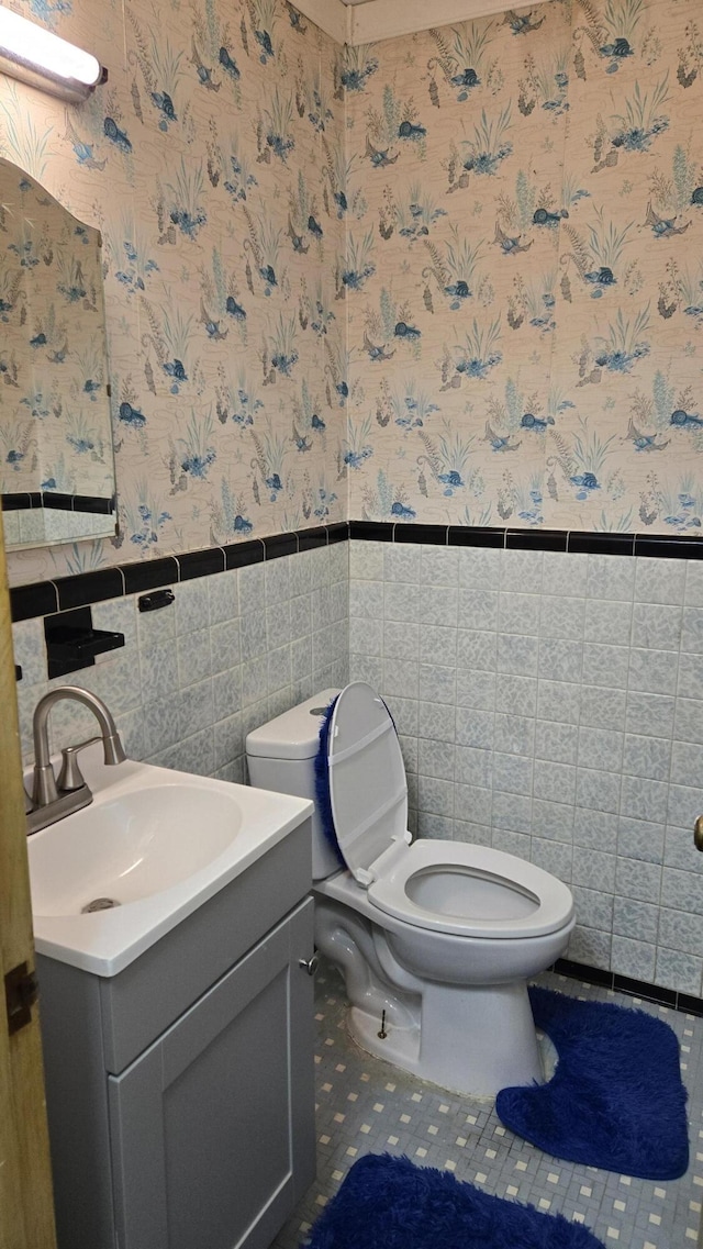 bathroom featuring toilet, wallpapered walls, and wainscoting