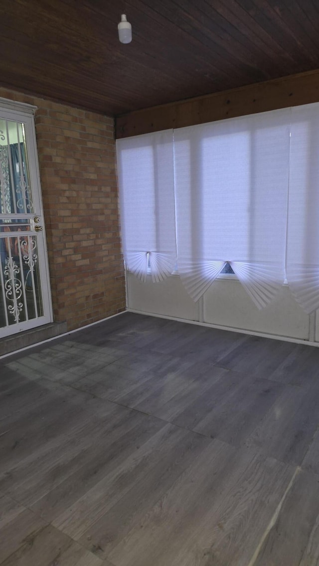 spare room with brick wall, wooden ceiling, and wood finished floors