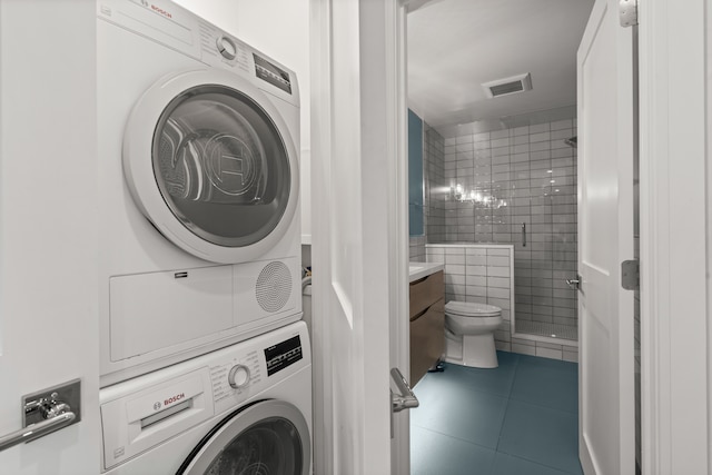 clothes washing area with dark tile patterned flooring, stacked washer and dryer, and tile walls