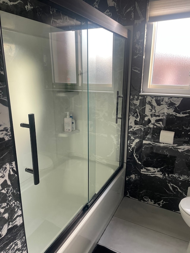 bathroom featuring combined bath / shower with glass door and toilet