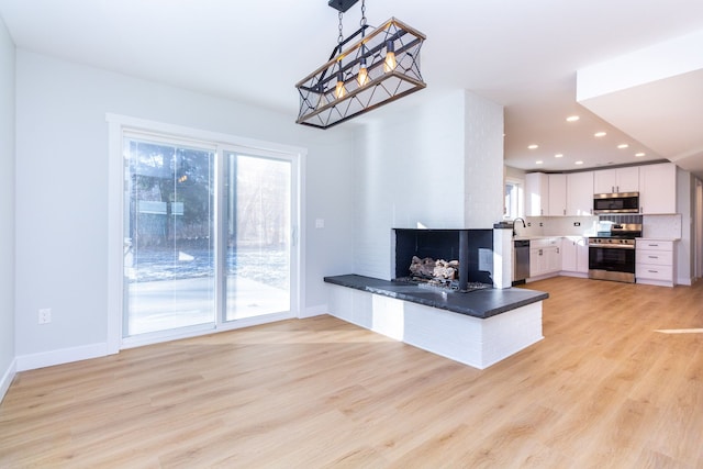 kitchen with hanging light fixtures, stainless steel appliances, backsplash, white cabinets, and light wood-type flooring