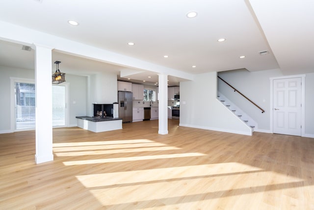 unfurnished living room with a multi sided fireplace, sink, light hardwood / wood-style flooring, and a notable chandelier