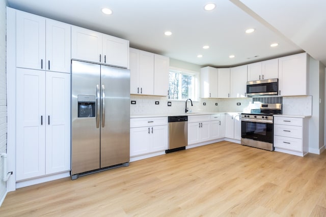 kitchen with tasteful backsplash, stainless steel appliances, sink, light hardwood / wood-style flooring, and white cabinets