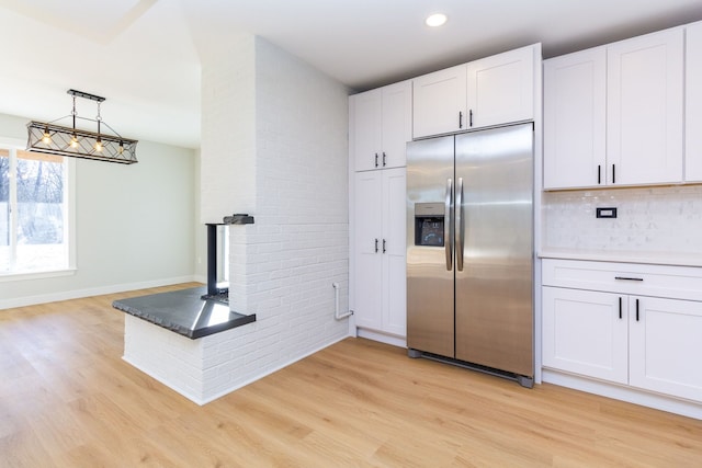 kitchen with pendant lighting, white cabinets, light hardwood / wood-style flooring, stainless steel fridge, and tasteful backsplash