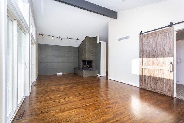 unfurnished living room featuring a barn door, beamed ceiling, high vaulted ceiling, dark hardwood / wood-style floors, and a fireplace