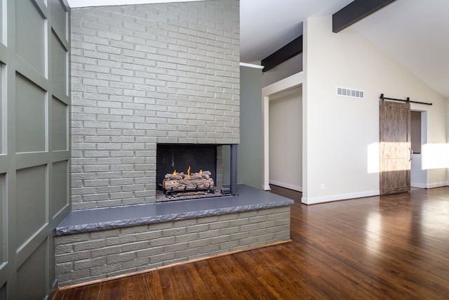 unfurnished living room with a brick fireplace, a barn door, vaulted ceiling with beams, built in features, and dark hardwood / wood-style floors