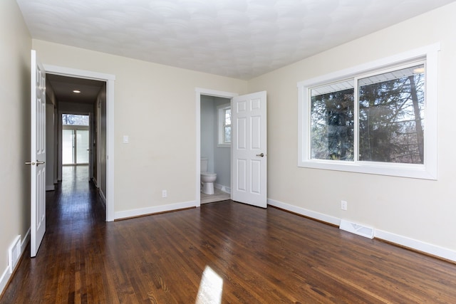 unfurnished bedroom with ensuite bathroom and dark hardwood / wood-style floors