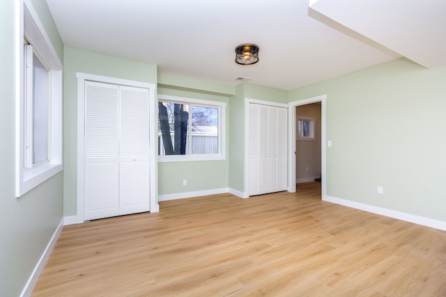 unfurnished bedroom featuring light hardwood / wood-style flooring and multiple closets