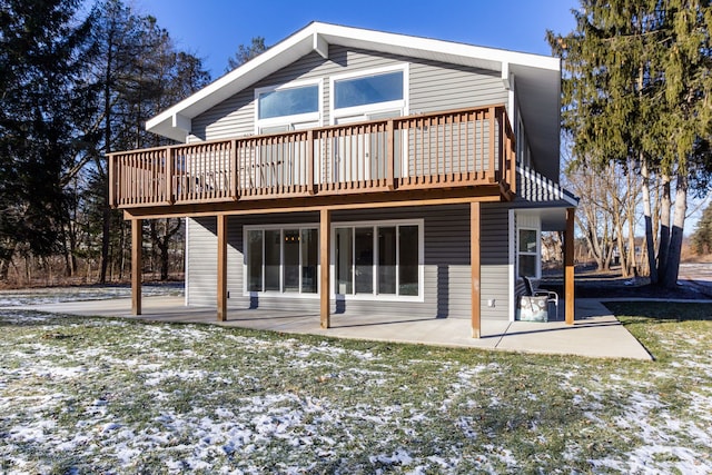 snow covered rear of property featuring a deck, a patio area, and a lawn