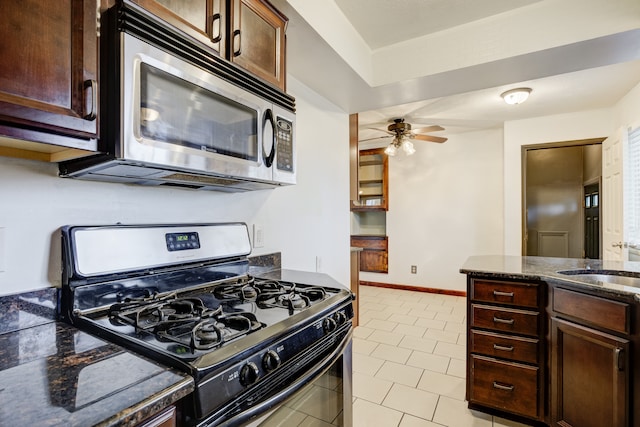 kitchen featuring black gas range, sink, ceiling fan, dark stone countertops, and dark brown cabinetry