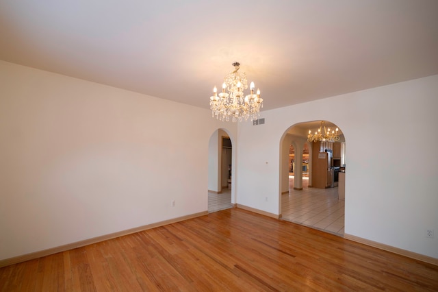 spare room with light hardwood / wood-style floors and a notable chandelier