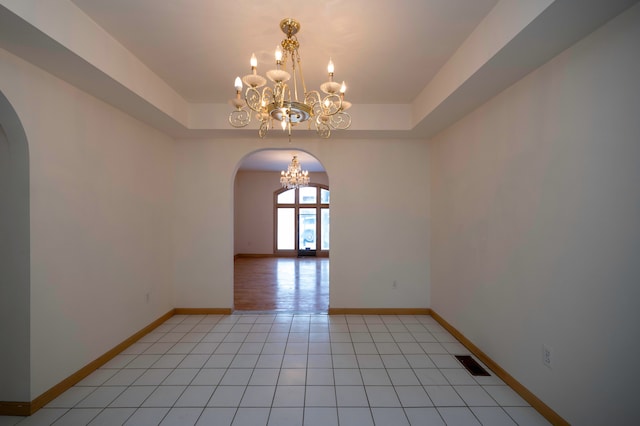 tiled empty room with an inviting chandelier and a tray ceiling