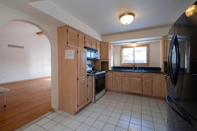 kitchen with sink, light tile patterned floors, black appliances, and light brown cabinets