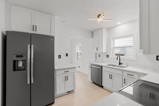 kitchen with white cabinetry, sink, stainless steel appliances, light stone counters, and a textured ceiling