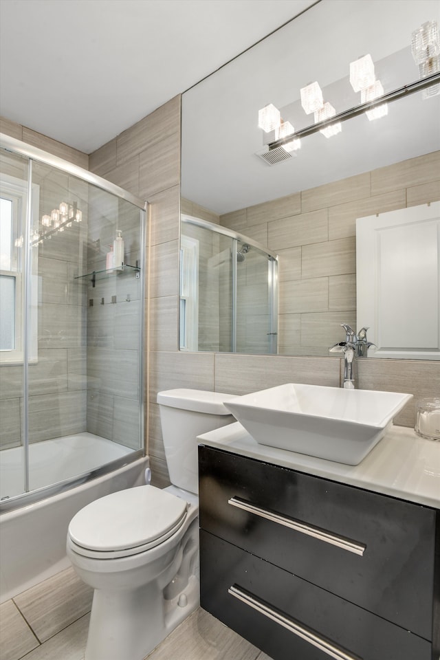 full bathroom featuring shower / bath combination with glass door, vanity, tile walls, and toilet