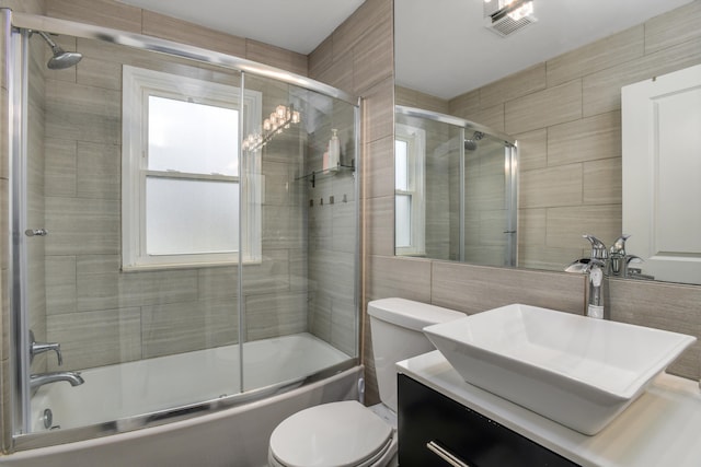 full bathroom with vanity, combined bath / shower with glass door, tile walls, and toilet