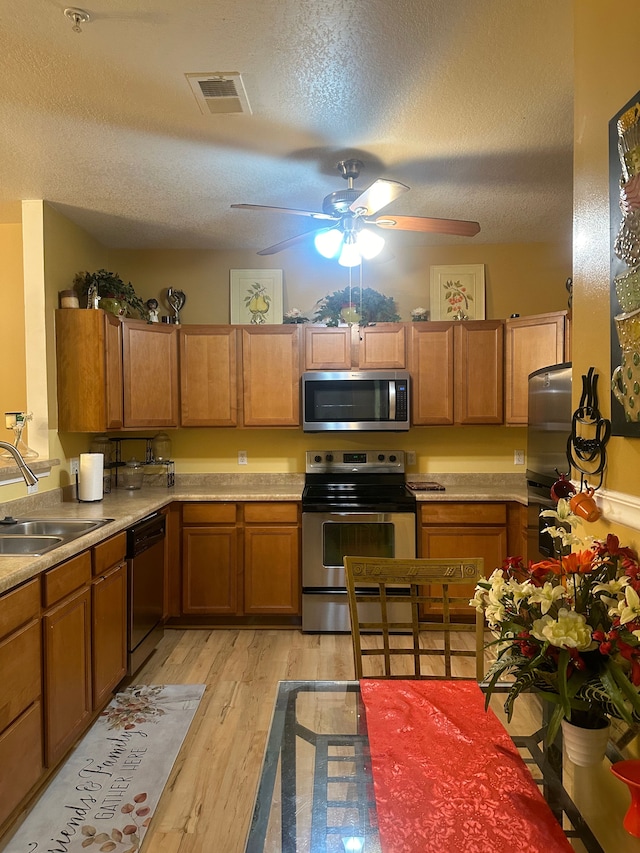 kitchen featuring sink, stainless steel appliances, a textured ceiling, and light hardwood / wood-style flooring