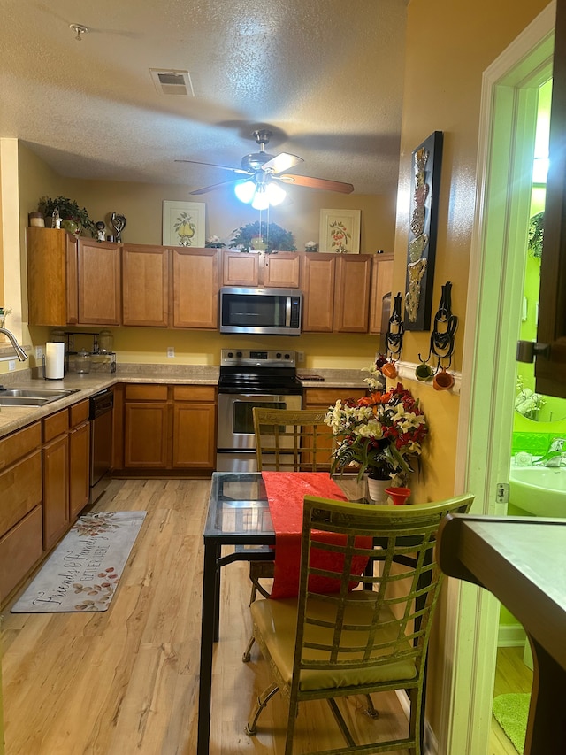 kitchen featuring light wood-type flooring, a textured ceiling, stainless steel appliances, ceiling fan, and sink