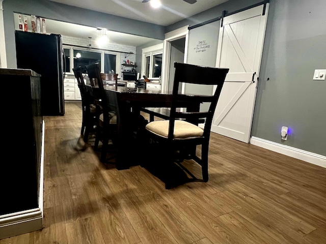 dining room with ceiling fan, wood-type flooring, and a barn door