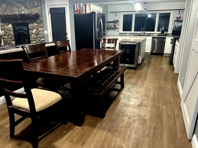 dining space featuring light wood-type flooring, beverage cooler, a stone fireplace, and sink