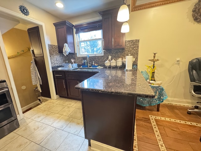 kitchen featuring hanging light fixtures, tasteful backsplash, dark stone countertops, dark brown cabinets, and light tile patterned flooring