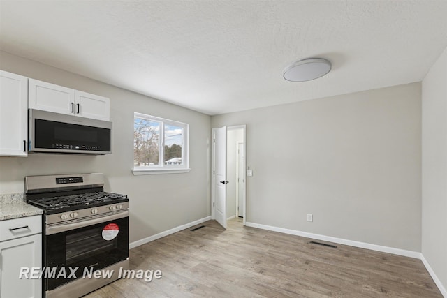 kitchen with white cabinets, stainless steel appliances, light stone countertops, and light hardwood / wood-style floors