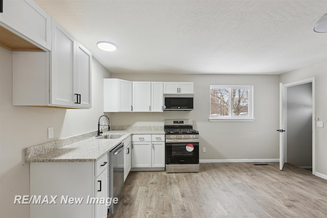 kitchen with appliances with stainless steel finishes, light hardwood / wood-style floors, white cabinetry, and sink