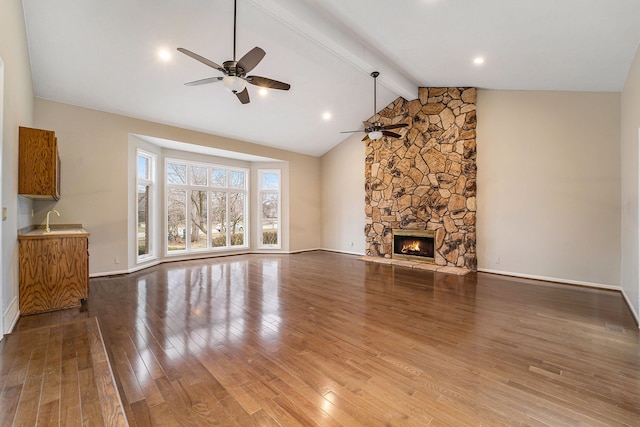 unfurnished living room featuring ceiling fan, sink, wood-type flooring, lofted ceiling with beams, and a fireplace