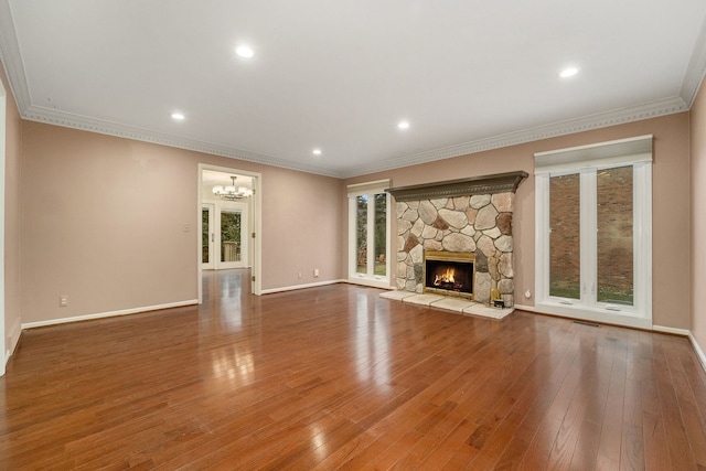 unfurnished living room featuring wood-type flooring, an inviting chandelier, a stone fireplace, and ornamental molding