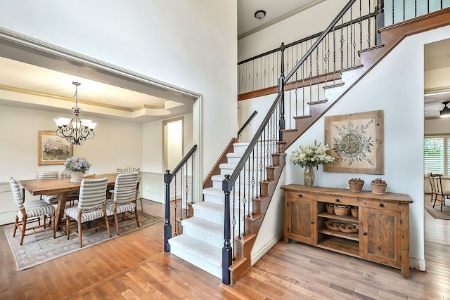 staircase with a raised ceiling, wood-type flooring, crown molding, and an inviting chandelier