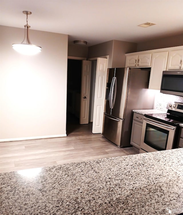 kitchen featuring white cabinets, hanging light fixtures, light wood-type flooring, light stone counters, and stainless steel appliances