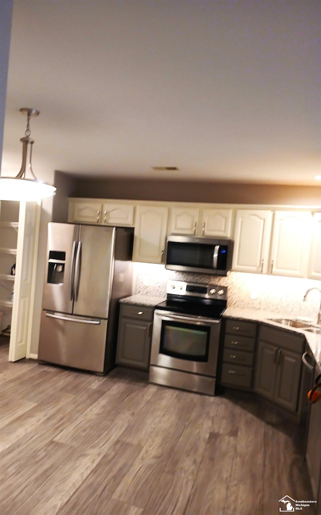 kitchen with light stone countertops, sink, stainless steel appliances, white cabinets, and hardwood / wood-style flooring