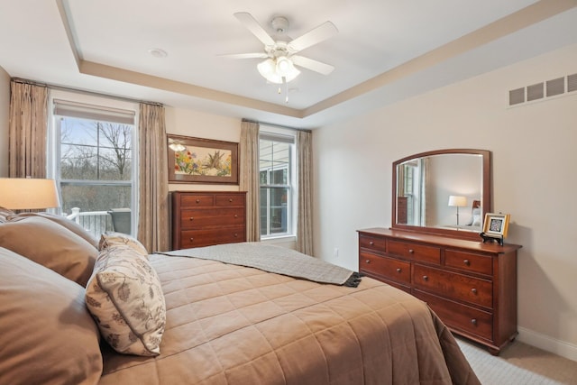 carpeted bedroom featuring a raised ceiling, multiple windows, and ceiling fan