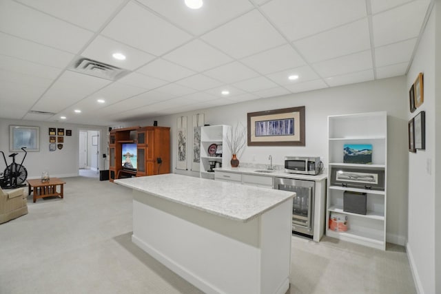 kitchen featuring a kitchen island, light colored carpet, sink, and beverage cooler