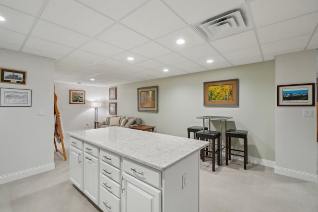 kitchen with a paneled ceiling, a center island, white cabinets, and light colored carpet