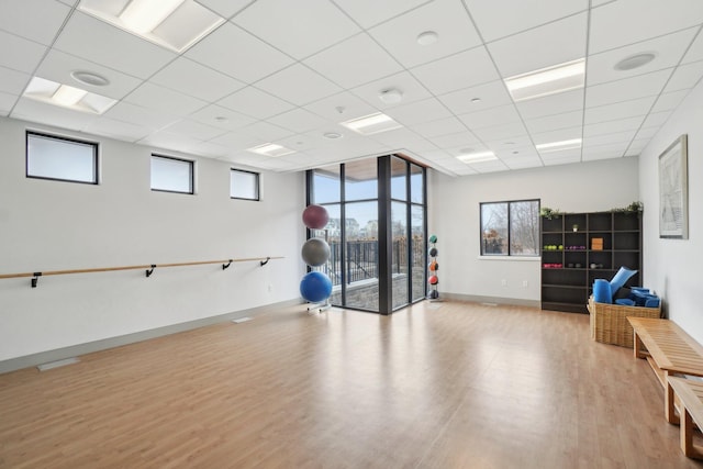 exercise room with a paneled ceiling, light hardwood / wood-style flooring, and a healthy amount of sunlight