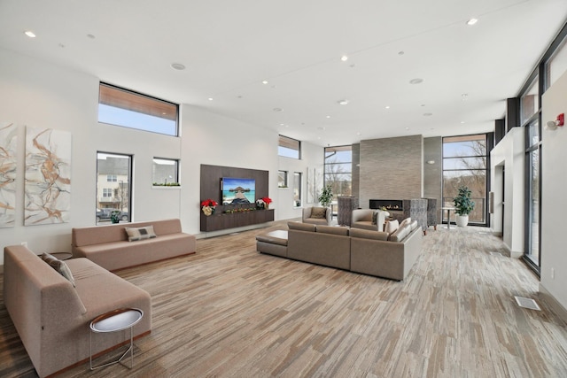 living room featuring a fireplace, light wood-type flooring, and a towering ceiling