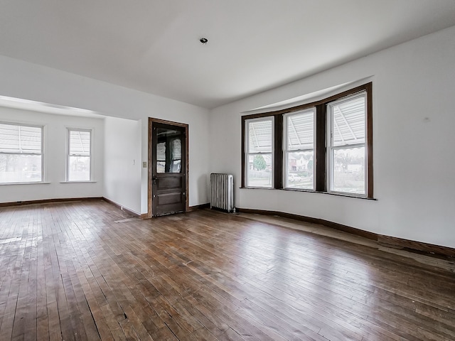 unfurnished room with radiator heating unit, dark wood-style floors, baseboards, and a wealth of natural light