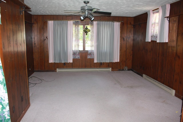 carpeted empty room with a textured ceiling, a baseboard radiator, ceiling fan, and wood walls