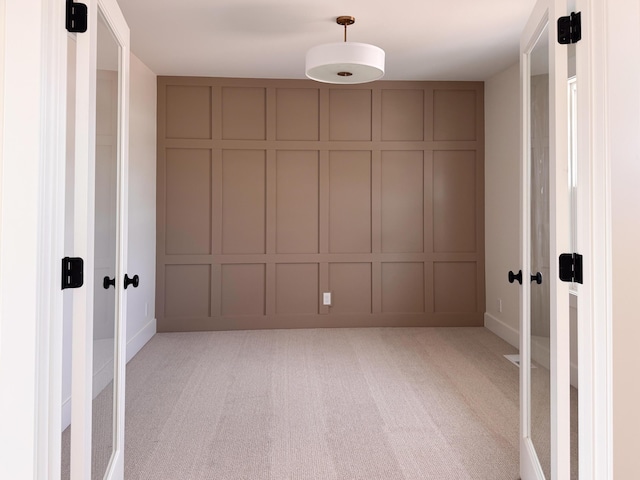 empty room with baseboards, light carpet, and a decorative wall