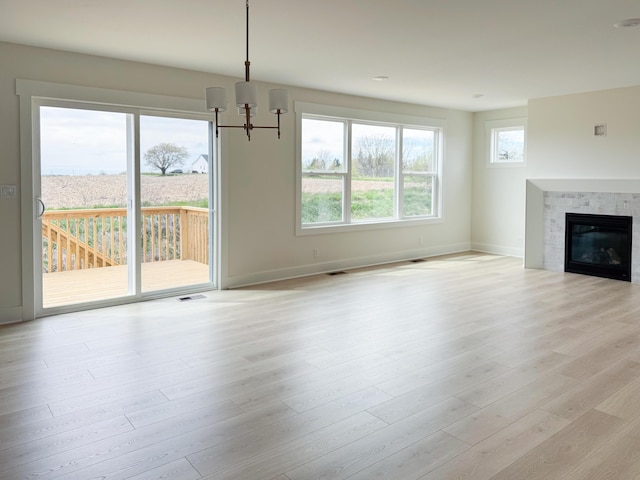 unfurnished living room with visible vents, a glass covered fireplace, baseboards, a chandelier, and light wood finished floors