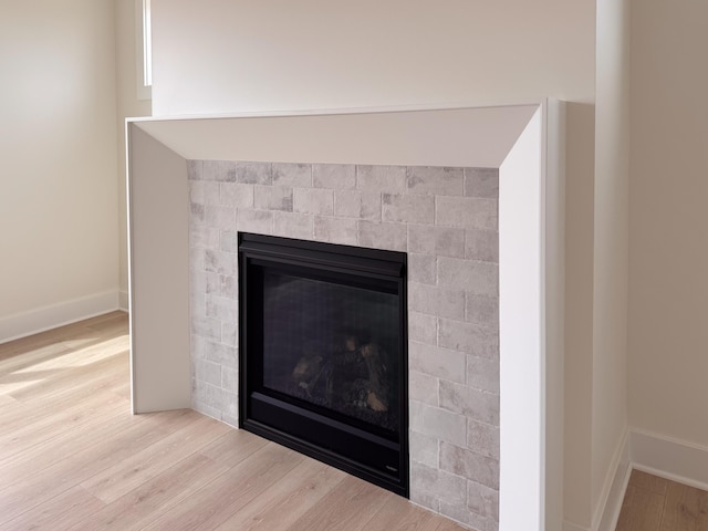 details featuring baseboards, a glass covered fireplace, and wood finished floors