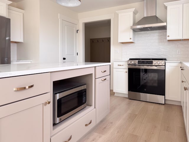 kitchen featuring light wood-style floors, light countertops, wall chimney exhaust hood, appliances with stainless steel finishes, and backsplash