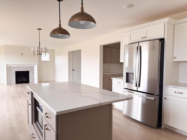 kitchen with pendant lighting, a center island, light stone countertops, light wood-style floors, and stainless steel appliances