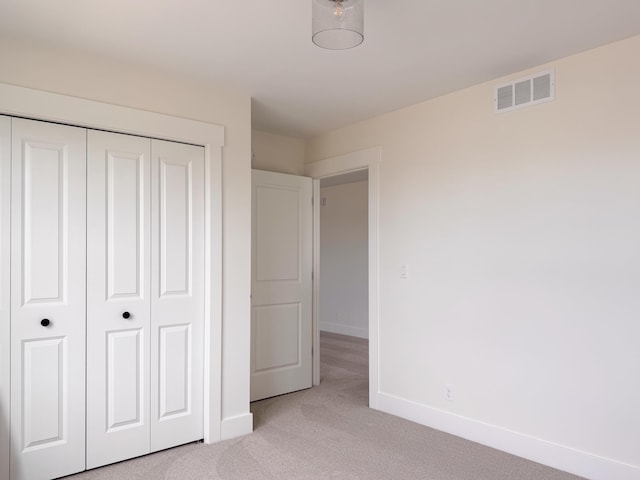 unfurnished bedroom featuring baseboards, light carpet, a closet, and visible vents
