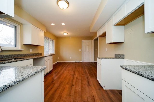 kitchen with sink, light stone countertops, a wealth of natural light, dark hardwood / wood-style flooring, and white cabinetry