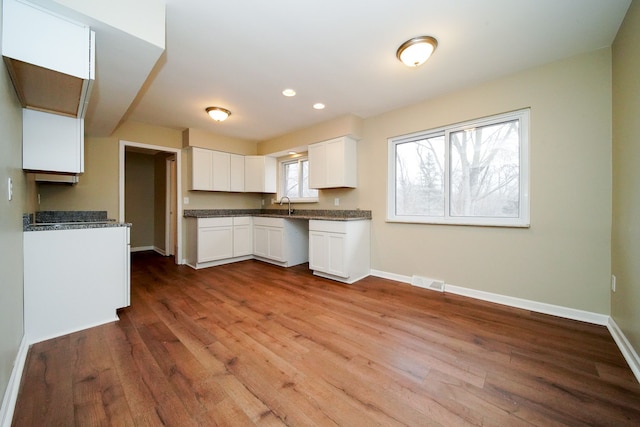 kitchen featuring white cabinetry, hardwood / wood-style floors, dark stone counters, and sink