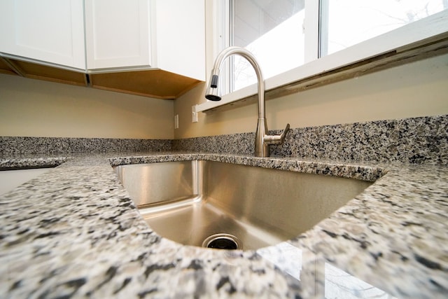 room details featuring white cabinets, light stone countertops, and sink