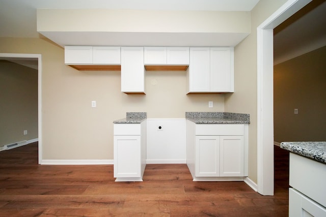 kitchen with light stone counters, white cabinetry, and wood-type flooring