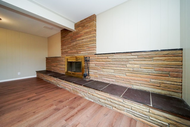 unfurnished living room with hardwood / wood-style floors, beam ceiling, and a stone fireplace